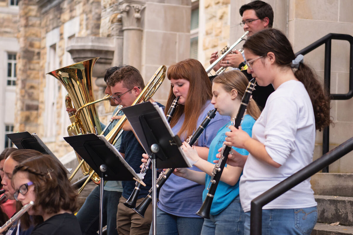 Student musicians playing brass and woodwinds on stone steps